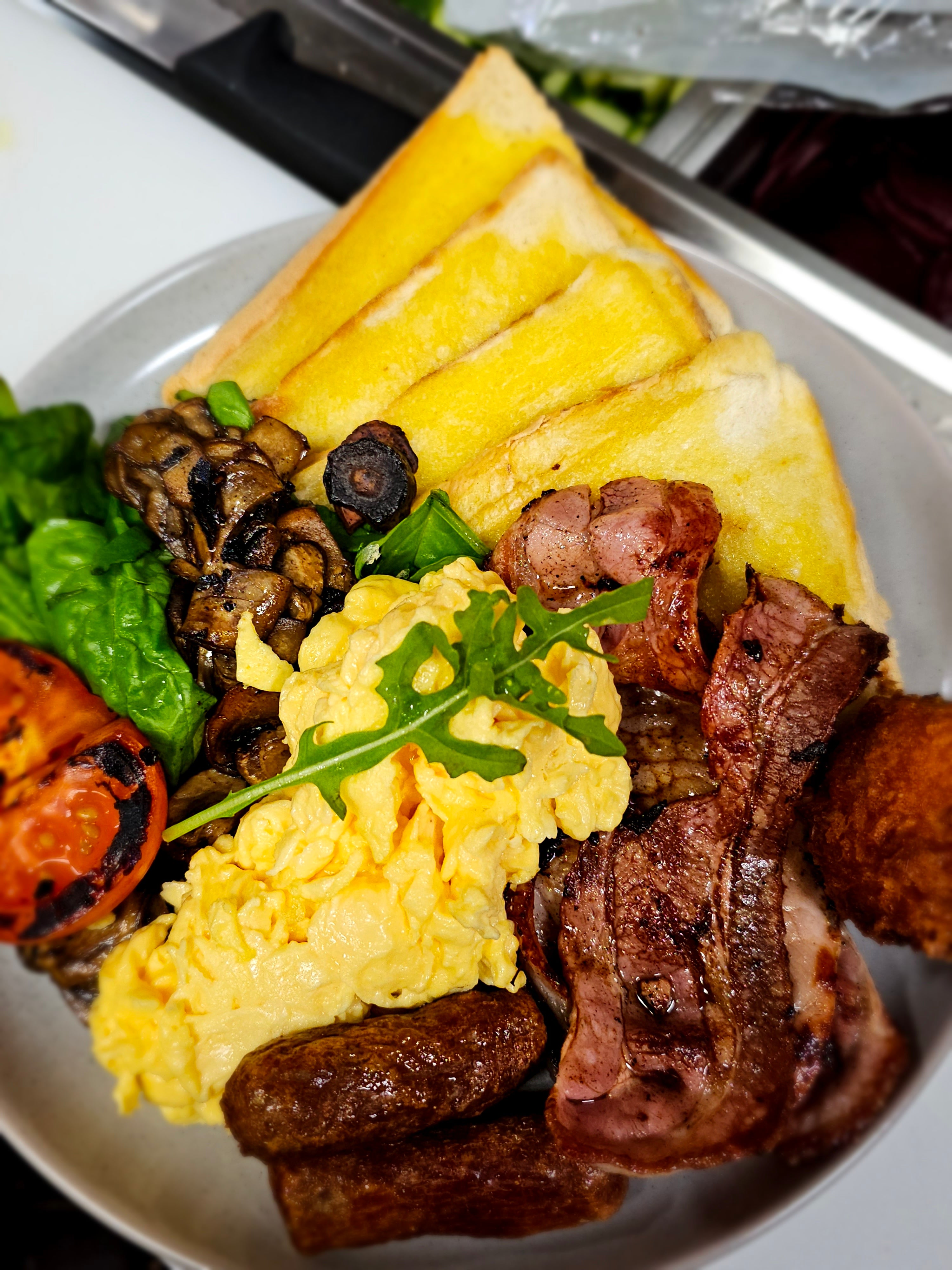 Bruce Almighty breakfast plate with bacon, eggs, chipolatas, hash brown, grilled mushrooms, spinach, grilled tomato, and toast at The Social Cafe in Emerald QLD 4720.